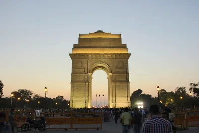 India Gate glowing in warm light at dusk with people on the avenue