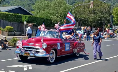 A vintage red car carrying flags in a small town parade