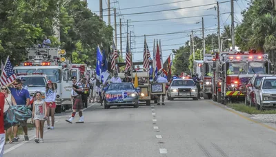 Fire trucks and marchers with flags coming down a town street