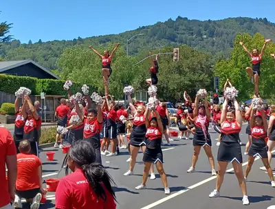 Cheerleaders in red lifting a teammate in a street parade
