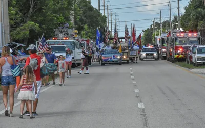 Families walking with flags behind fire trucks in a parade