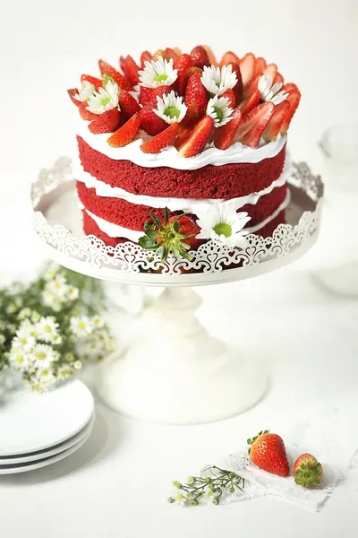 A red velvet layer cake topped with strawberries and daisies