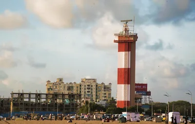 A red and white lighthouse above a busy beach road with buildings