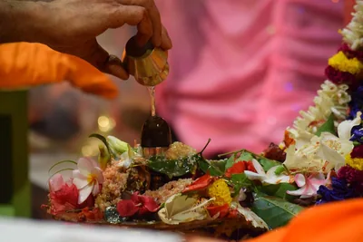 A hand offering items on a plate full of flowers and leaves during worship