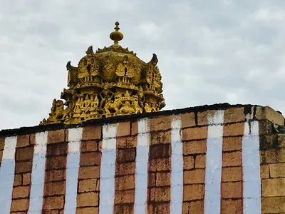 A golden temple tower above a wall painted with red and white stripes