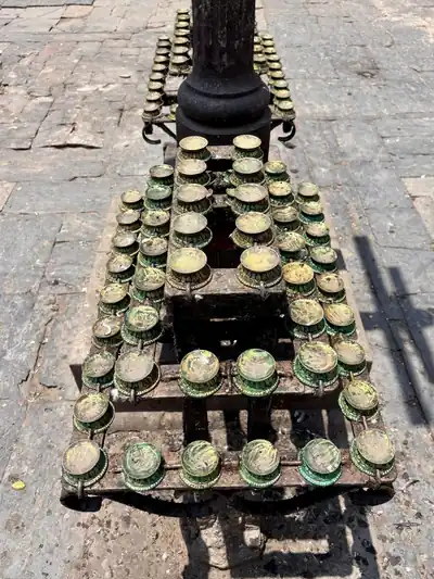 Rows of small brass lamp cups on a tiered iron stand on a stone floor