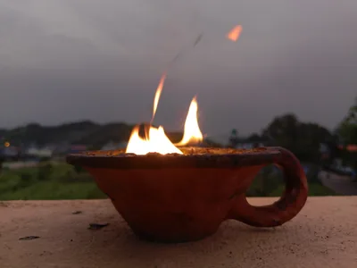 A clay lamp with a bright flame on a wall at dusk with hills behind