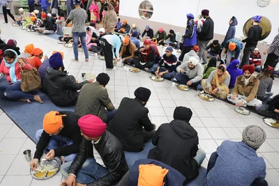 Many people seated on the floor sharing a meal in a large hall
