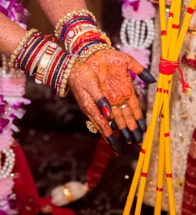 A bride's hand with mehendi, red and white bangles and a red thread