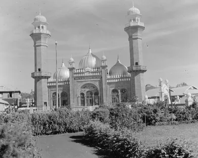 Old black and white photo of a domed mosque with minarets behind gardens