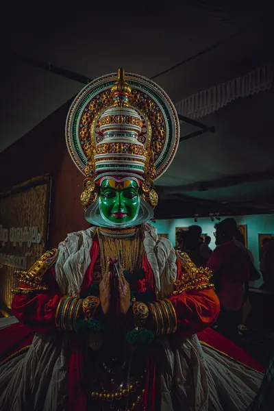 A Kathakali dancer with a green painted face and a tall gold crown
