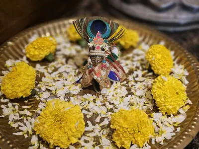 A small Krishna idol with a peacock feather crown on a bed of marigolds and white flowers