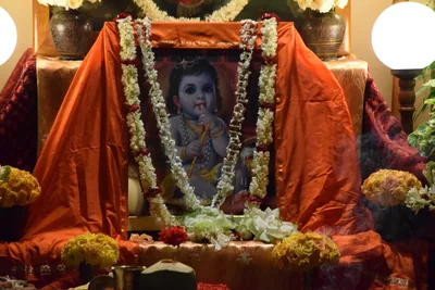 A picture of baby Krishna wrapped in garlands of white flowers and orange cloth