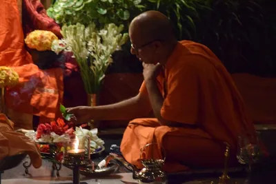 A monk in orange robes offering flowers before a lamp