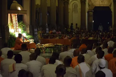 Rows of devotees in white sitting in a pillared temple hall