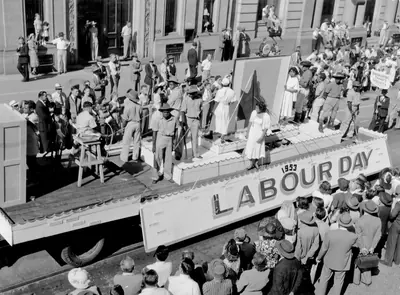Crowds watching a decorated truck float in an old May Day parade