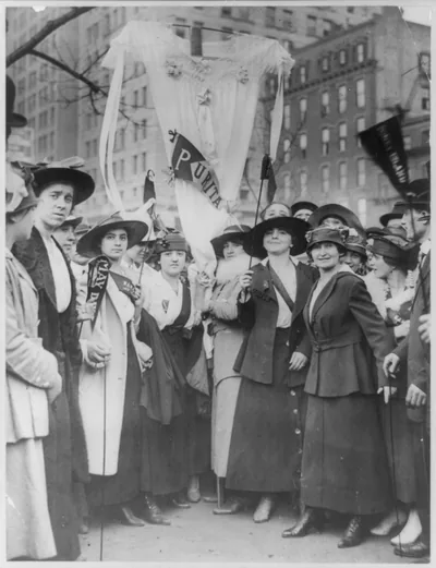 Women in hats and long coats marching with banners