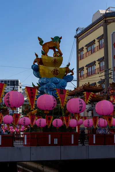 A giant lantern figure stands above rows of pink lanterns in a city street