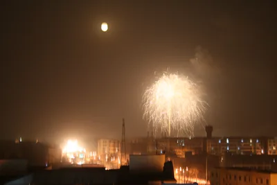 Fireworks burst under a bright full moon above a city at night