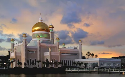 A white mosque with a golden dome under an evening sky