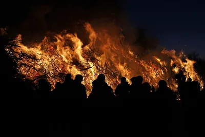 Dark outlines of people standing in front of a roaring bonfire