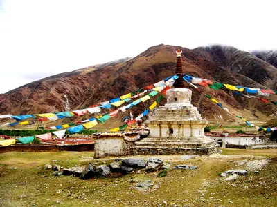 A white stupa with strings of colourful prayer flags below brown hills