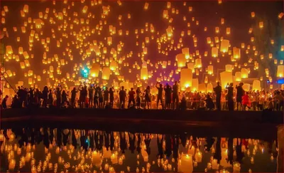 Hundreds of glowing paper lanterns rise into the night sky above a crowd by the water