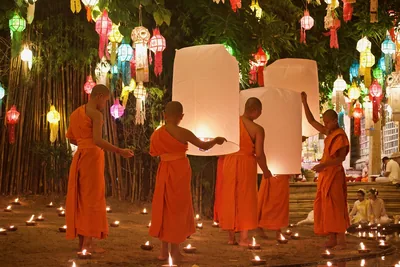 Monks in orange robes release large white paper lanterns among candles and hanging lamps