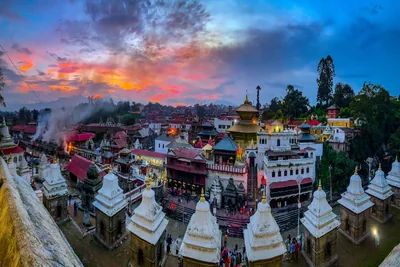 A temple complex with white shrines and golden roofs under a colourful sunset sky