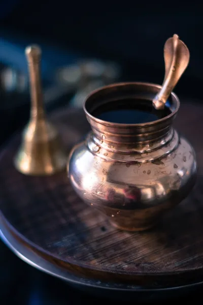 A shining copper water pot with a spout beside a brass bell