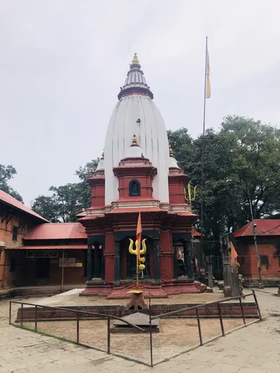 A white temple tower with a trident and red shrines around a courtyard