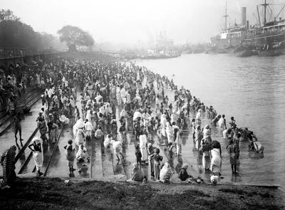 An old photograph of a large crowd bathing and praying on the river bank