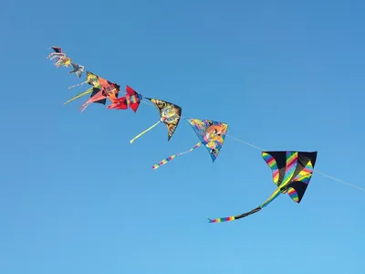 A long train of colourful kites flying in a clear blue sky