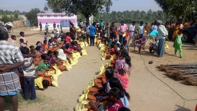 People seated along a row of clay pots, cooking on an open ground