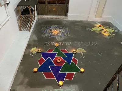 A colourful kolam with small oil lamps at a doorstep