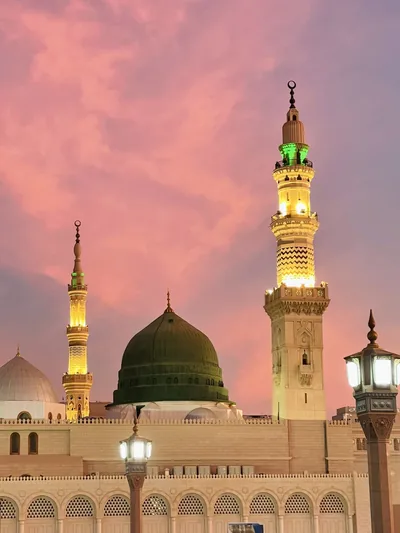 The green dome and lit minaret of the Prophet's Mosque in Madinah under a pink evening sky