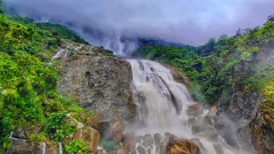 A tall waterfall pours down a green cliff under mist