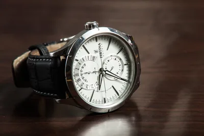 A silver wristwatch with a white dial on a wooden table