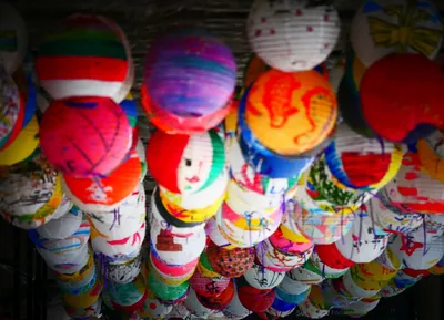Many round paper lanterns painted in bright colours hanging close together