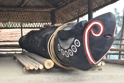 A carved Ao Naga log drum with white spiral patterns under a shelter