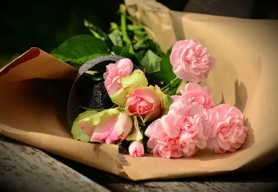 A bouquet of pink roses and carnations wrapped in brown paper