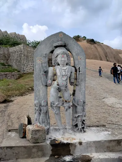 A standing stone deity under a carved arch on a rocky hilltop