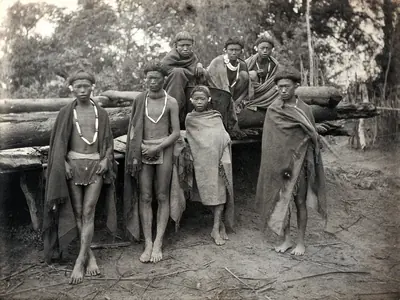 Old photograph of Naga men in shawls and bead necklaces outside a house