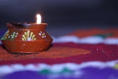 A painted clay diya burning beside colourful rangoli powder