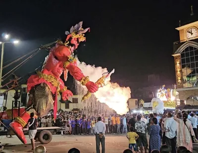 A tall painted effigy of Narakasura stands at night as a crowd watches