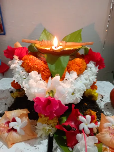 A brass kalash topped with a lamp and surrounded by marigolds and white flowers