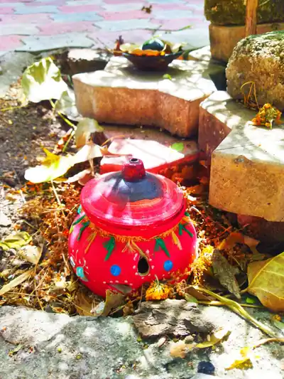 A hand-painted red clay garbo pot with holes, set among dry leaves