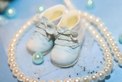 A pair of soft white baby shoes on a pale blue cloth with pearls