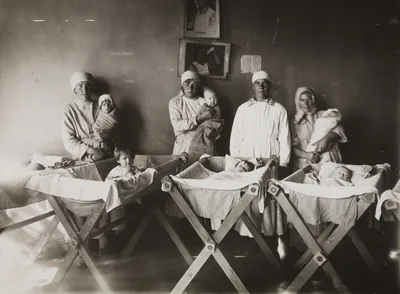 An old photo of nurses in a hospital nursery with rows of baby cradles