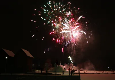 Red and white fireworks over a waterfront with lamps and wooden houses